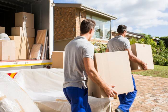 Movers carrying packed boxes from a truck toward a home