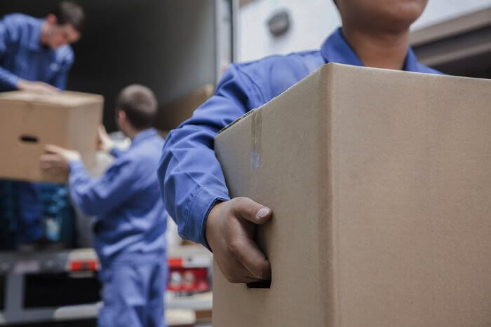 Movers carrying cardboard boxes beside a moving truck